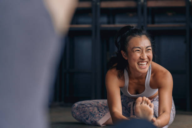 Casual conversations during warm up before the yoga session Young adult yoga practitioners have a casual conversation during warm up for a yoga session fitness trainer stock pictures, royalty-free photos & images