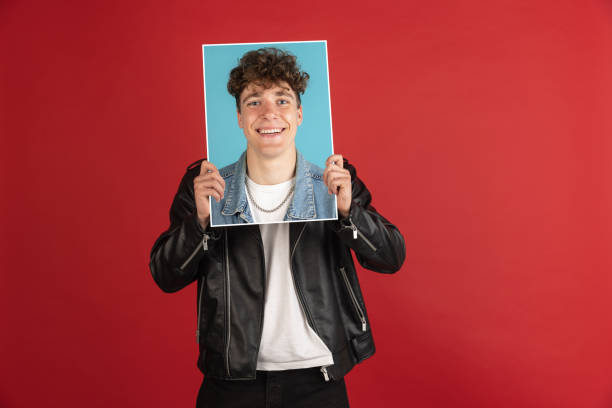 istock Young man holding his portrait isolated over red studio background with copyspace for ad. 1324176549