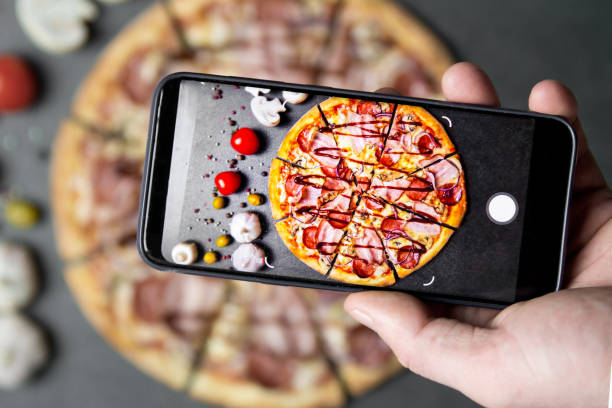 istock Using mobile phone to photograph the Pizza . Pizza with ingredients on a stone table top view. 1324178268