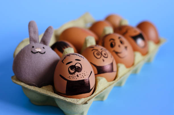 istock Creative Easter eggs with Corona virus (COVID19) protection concepts. Chicken eggs with pills on mini shopping cart with doodle faces wearing medical masks on blue background. Flat lay, DIY. 1324180290