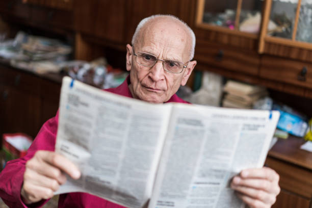 istock Serious elderly grey haired man wearing eyewear reading newspaper 1324185338