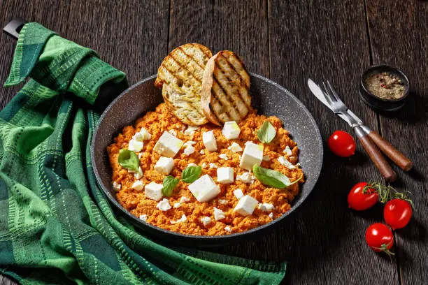 Strapatsada, eggs scrambled with tomatoes and feta cheese in a skillet with toasted bread, horizontal view from above, greek cuisine