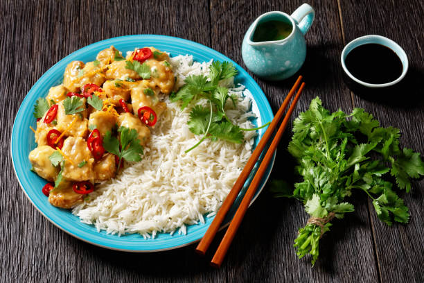 istock Mango glazed spicy chicken breast chunks with rice on a blue plate with chopsticks, on a dark wooden table, horizontal view from above 1324186914
