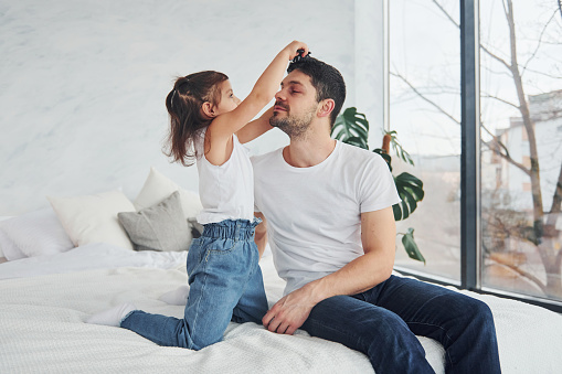 Happy father with his daughter having fun with comb at home together.