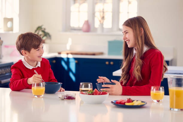 frère et sœur portant l’uniforme scolaire dans la cuisine manger un petit déjeuner sain - healthy lifestyle people eating sister photos et images de collection