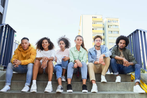 istock Group of young people sitting in a row on the stairs 1324190877