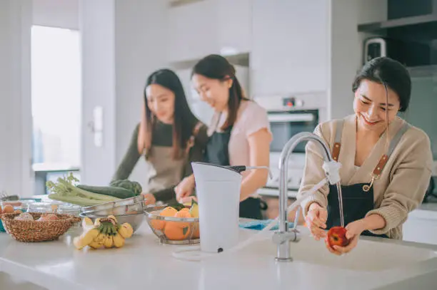 Photo of 3 asian chinese female friends preparing food cooking at home during weekend at kitchen counter