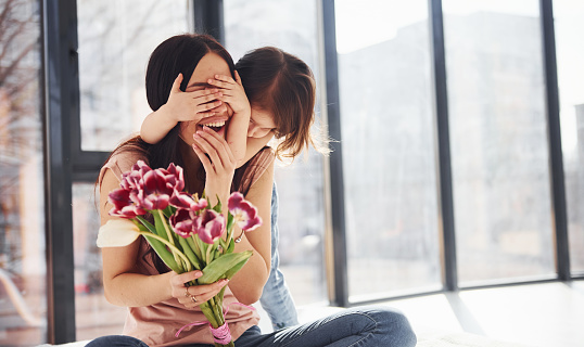 Covering eyes. Daughter congratulates mother with holiday and gives bouquet of flowers.