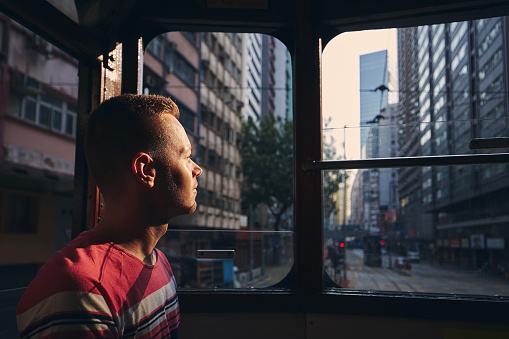 Pensive man looking out old tram window. Tourist exploring  city streets of Hong Kong.