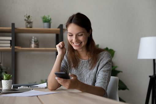 Excited woman reading good news, using smartphone, showing yes gesture, happy young businesswoman looking at phone screen, celebrating success, received job promotion or reward, business achievement