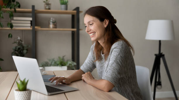istock Smiling woman using laptop, sitting at desk, having fun 1324194660