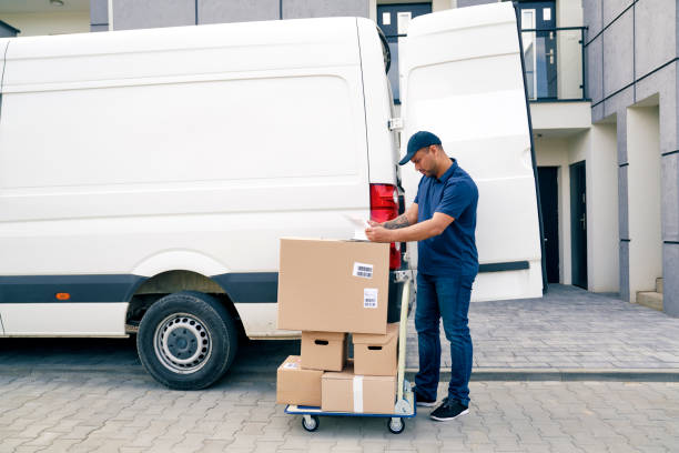 istock Courier with packages on a hand truck looking at documents 1324195274