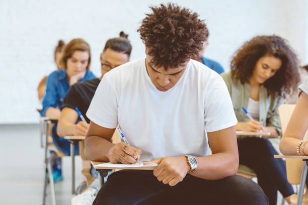 istock Young man writing exam at desk in classroom 1324197392