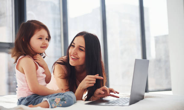 istock Young mother with her daughter spending weekend together in room and using laptop 1324197538