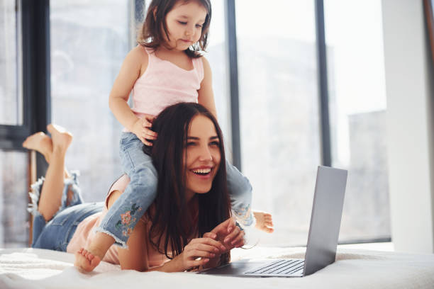 istock Young mother with her daughter spending weekend together in room and using laptop 1324197627