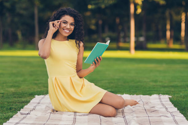 portret atrakcyjnej inteligentnej wesołej dziewczyny siedzącej na kołdrę czytając ciekawą książkę wolny czas studiuje na �świeżym powietrzu na świeżym powietrzu na świeżym powietrzu - book reading dress women zdjęcia i obrazy z banku zdjęć