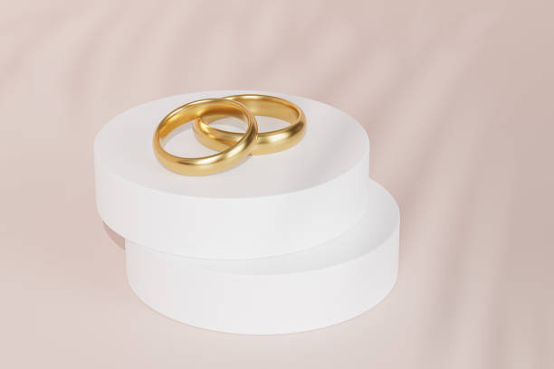 istock Two golden wedding rings on white podium or pedestal, beige background with leaf shadow, 3d render 1324202471