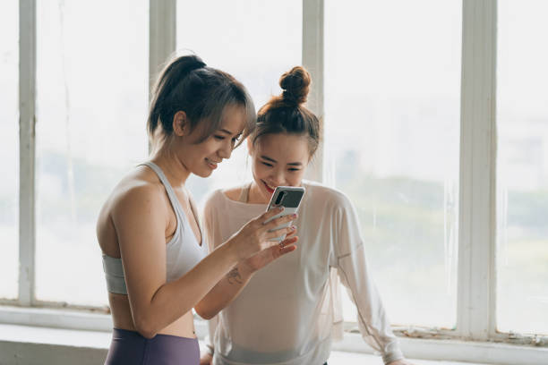 zwei asiatische frauen, die ein mobiltelefon überprüfen - photographing smart phone friendship photo messaging stock-fotos und bilder