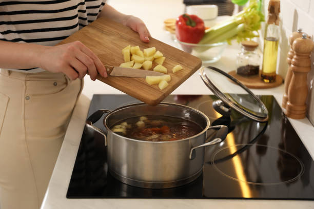 femme mettant des pommes de terre dans le pot pour faire du bouillon dans la cuisine, gros plan. recette maison - making soup photos et images de collection