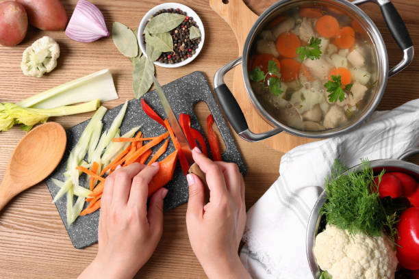 istock Woman cutting vegetables for bouillon at wooden table, top view 1324207372