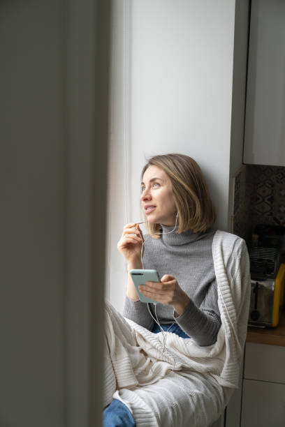 istock Smiling Woman Looking Away While Sitting By Window With Smart Phone 1324210459