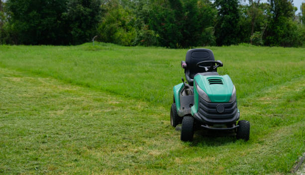 grünes gras trimmen mit rasenmäher. traktor mäht gras in einem öffentlichen park. ein schmutziger rasentraktor nach dem mähen des rasens steht auf der wiese. professioneller rasenmäher schneidet das gras. - lawn mower tractor gardening riding mower stock-fotos und bilder