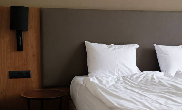 istock Close-up fragment of bedroom with empty bedside table, reading lamp and a USB socket in modern interior​ design home or hotel. Soft pillow and blanket, stylish comfortable furniture. 1324211668