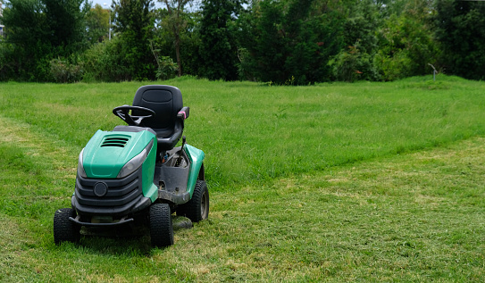 Mature man pushing a lawnmower round a lawn in front of cottage.