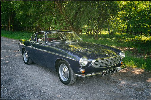 Stokenchurch, UK - June 14, 2021: A classic dark blue Volvo 1800S from 1967 sitting in a rural scene in the English countryside. Made famous when a white version was used by Roger Moore in the iconic sixties tv show The Saint, this svelt Swedish sports coupe is still a head-turner to this day.