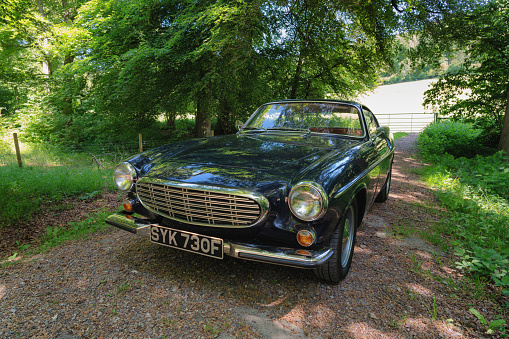 Stokenchurch, UK - June 14, 2021: A classic dark blue Volvo 1800S from 1967 sitting in a rural scene in the English countryside. Made famous when a white version was used by Roger Moore in the iconic sixties tv show The Saint, this svelt Swedish sports coupe is still a head-turner to this day.