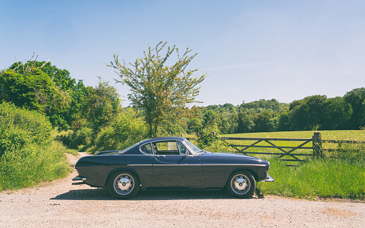 Stokenchurch, UK - June 14, 2021: A classic dark blue Volvo 1800S from 1967 sitting in a rural scene in the English countryside. Made famous when a white version was used by Roger Moore in the iconic sixties tv show The Saint, this svelt Swedish sports coupe is still a head-turner to this day.