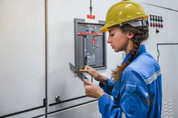 Female engineer with yellow hard hat helmet and holding tablet working inside factory stock photo