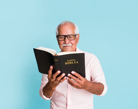 A happy senior latin man reading the bible.
