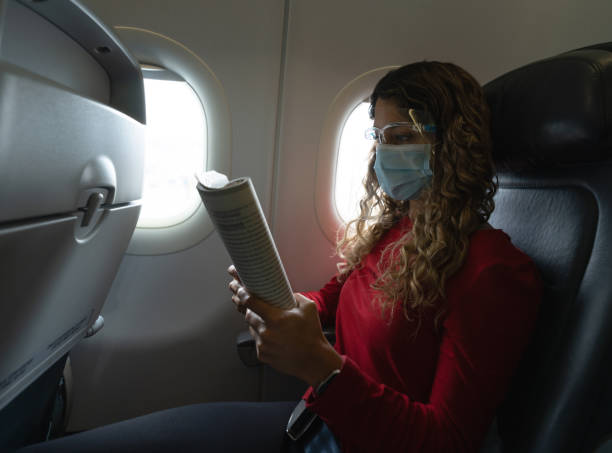 istock Traveler wearing a facemask with a face shield in the airplane while reading 1324227663