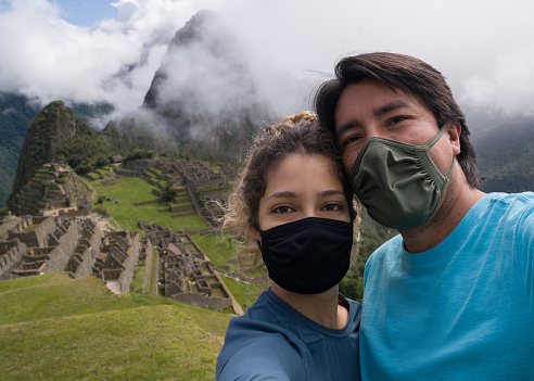 Portrait of a loving Latin American couple traveling to Machu Picchu during the pandemic and wearing facemasks - travel concepts