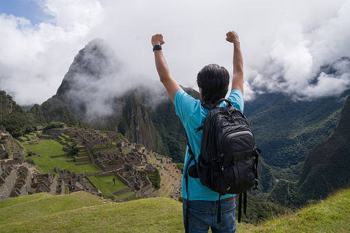 Happy man in Machu Picchu celebrating reaching the top of a mountain and looking at the view - tourism concepts