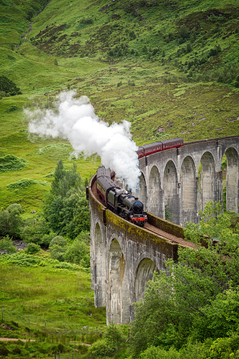 A vintage steam train crosses the Glenfinnan Viaduct at Loch Shiel, Scottish Highlands, UK. The West Highland line runs through Inverness-shire, Scotland.