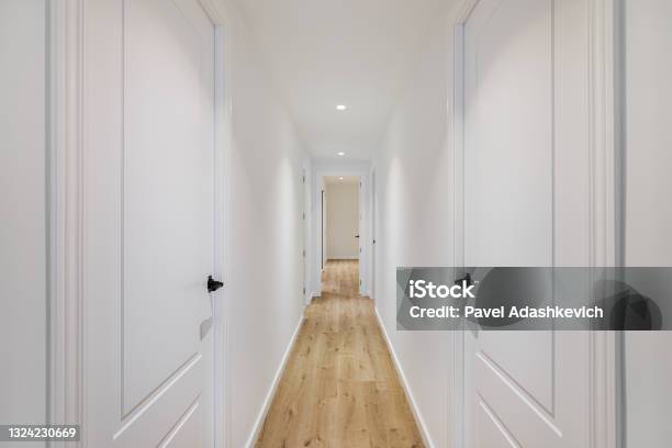 Interior Of Long Narrow Hallway With Closed Doors Wooden Floor And White Walls In Apartment Designed In Minimal Style Stock Photo - Download Image Now