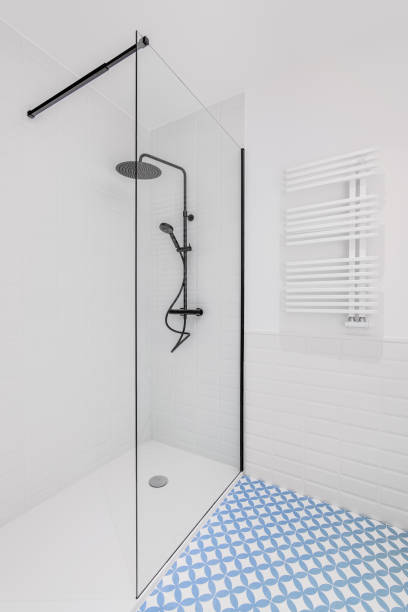 istock Bathroom decorated with light blue and white tiles. Modern shower zone with big rain head, hand held shower and glass door. 1324230676
