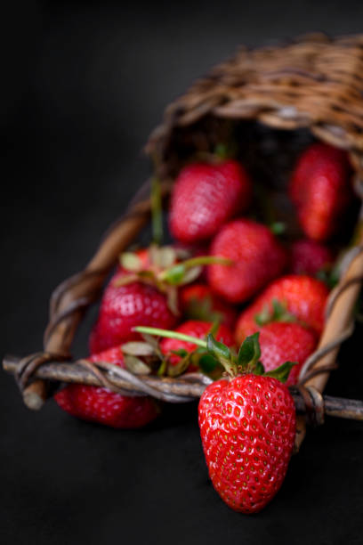 istock Ripe red strawberries scattered from wicker basket, dark background, close up 1324230756