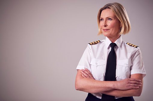 Studio Portrait Of Serious Mature Female Airline Pilot Against Plain Background