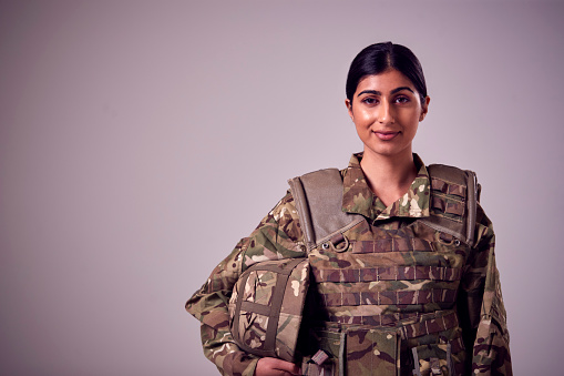 Retrato de estudio de una joven soldado sonriente con uniforme militar sobre un fondo llano photo