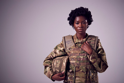 Retrato de estudio de una joven soldado seria con uniforme militar sobre un fondo llano photo