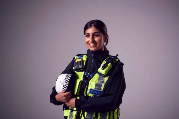 Studio Portrait Of Smiling Young Female Police Officer Against Plain Background