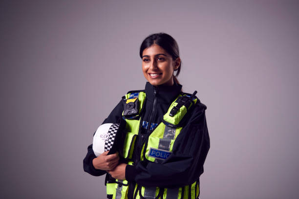 studio portrait of smiling young female police officer against plain background - polis kuvveti stok fotoğraflar ve resimler