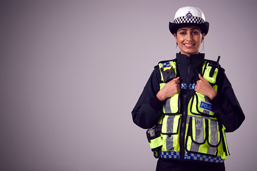 Studio Portrait Of Smiling Young Female Police Officer Against Plain Background