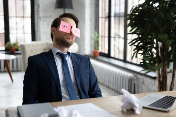 Exhausted bored manager sleeping with comic paper notes on eyes Exhausted bored manager sleeping at workplace with comic paper notes on eyes. Sleepy lazy employee relaxing on chair, feeling fatigue, overworked, low energy level, practicing stress reduce man sleeping chair stock pictures, royalty-free photos & images