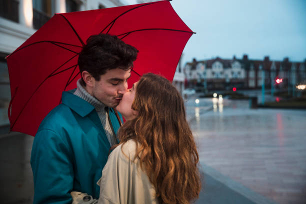 Photo of a mother and daughter enjoying a rainy day outdoors, exchanging smiles, glances, and kisses while wearing their colorful raincoats