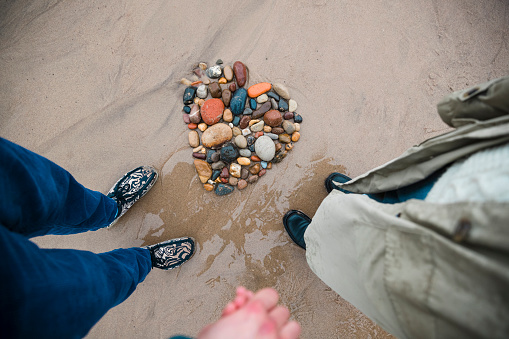 High angle view of an unrecognisable couple holding hands while standing at the beach in Whitley Bay, they are standing next to a heart shape they've made out of rocks and pebbles.
