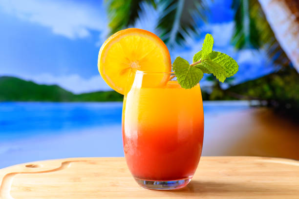 A GLASS OF COCKITEL SUNRISE AGAINST THE BACKGROUND OF A BEACH PARADISE SUMMER SUN A GLASS OF COCKITEL SUNRISE AGAINST THE BACKGROUND OF A BEACH PARADISE SUMMER SUN tequila sunrise stock pictures, royalty-free photos & images